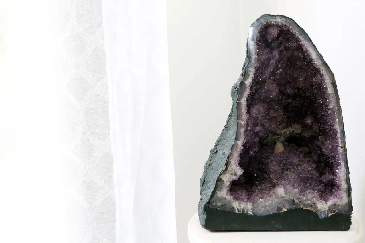 Géode d'améthyste ouverte exposée sur socle blanc, cristaux violets visibles à l'intérieur de la roche.